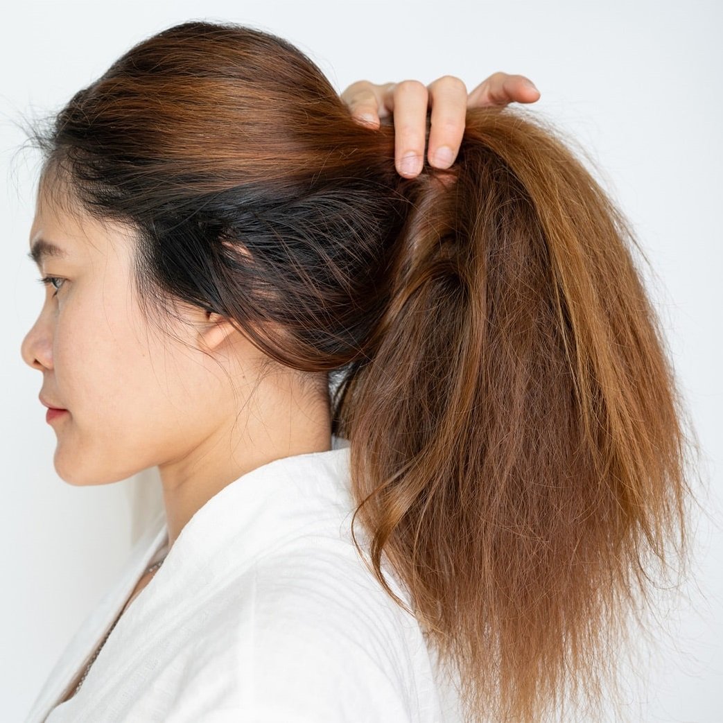A person pulling their dry, frizzy hair into a ponytail.